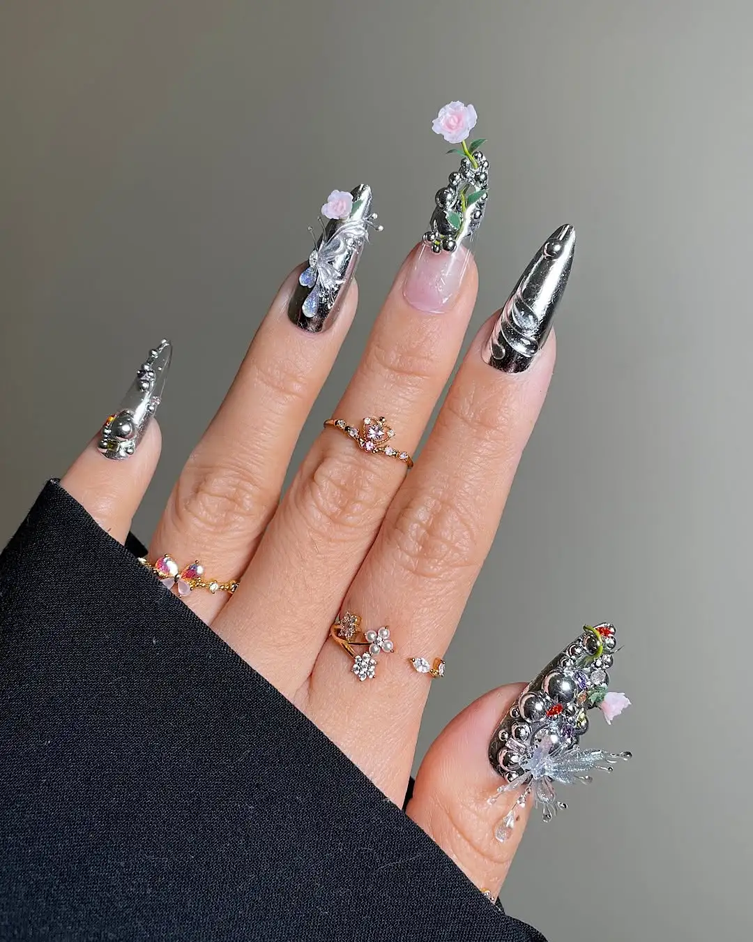 A manicured hand with ornate nail art featuring metallic details and floral decorations adorned with rings