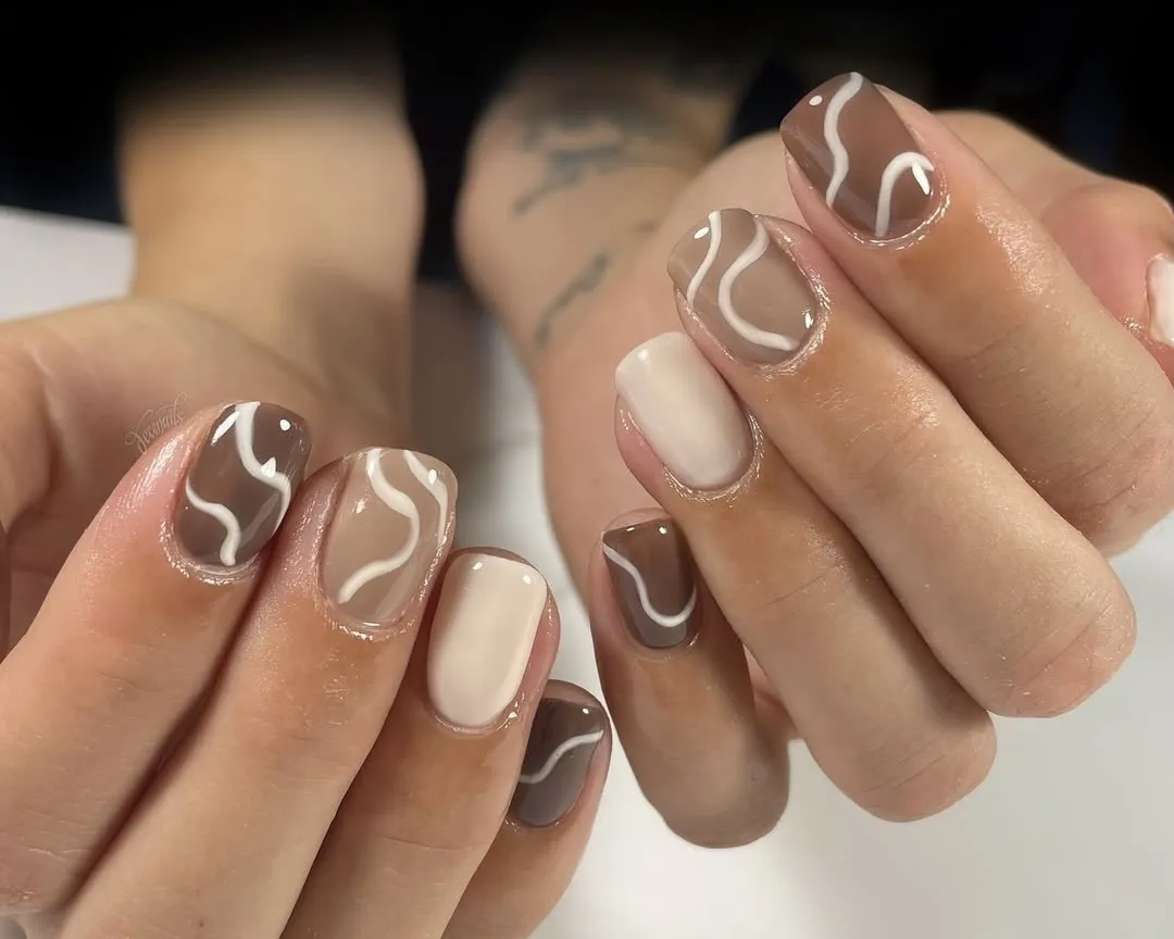 White, sandy, and brown gingerbread manicure with white abstract swirls.
