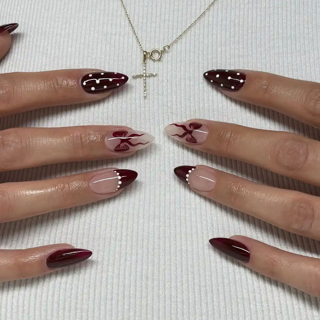 Almond-shaped nails with burgundy bows, polka dots, and French tips