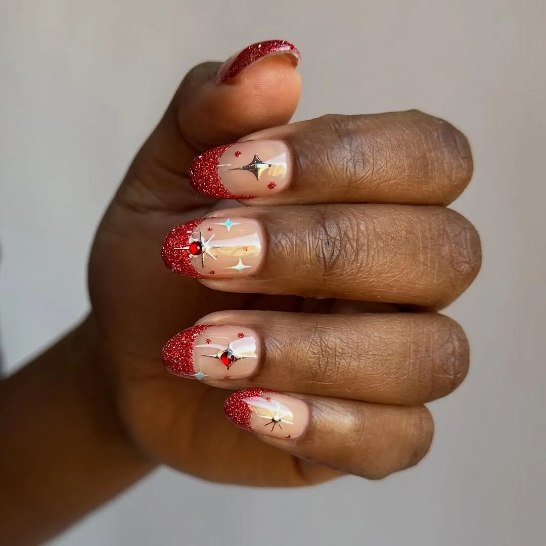 A persons hand adorned with red glittered nails and decorative designs on the nail tips closeup view