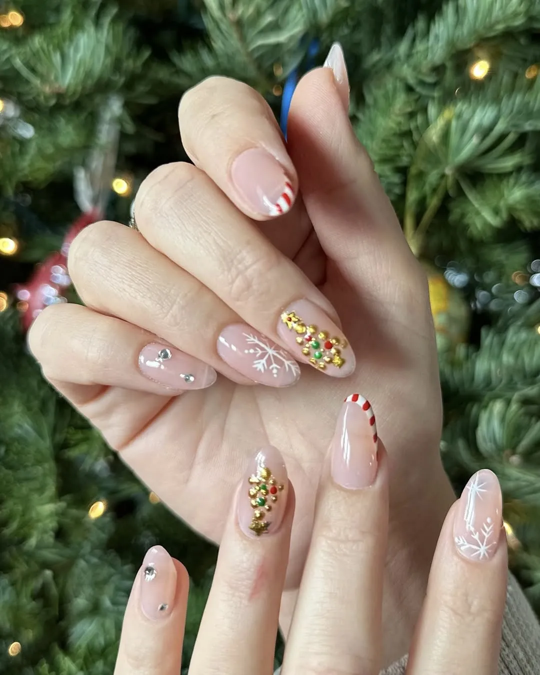 Nude Christmas nails with gold tree accents, snowflakes, and peppermint tips.