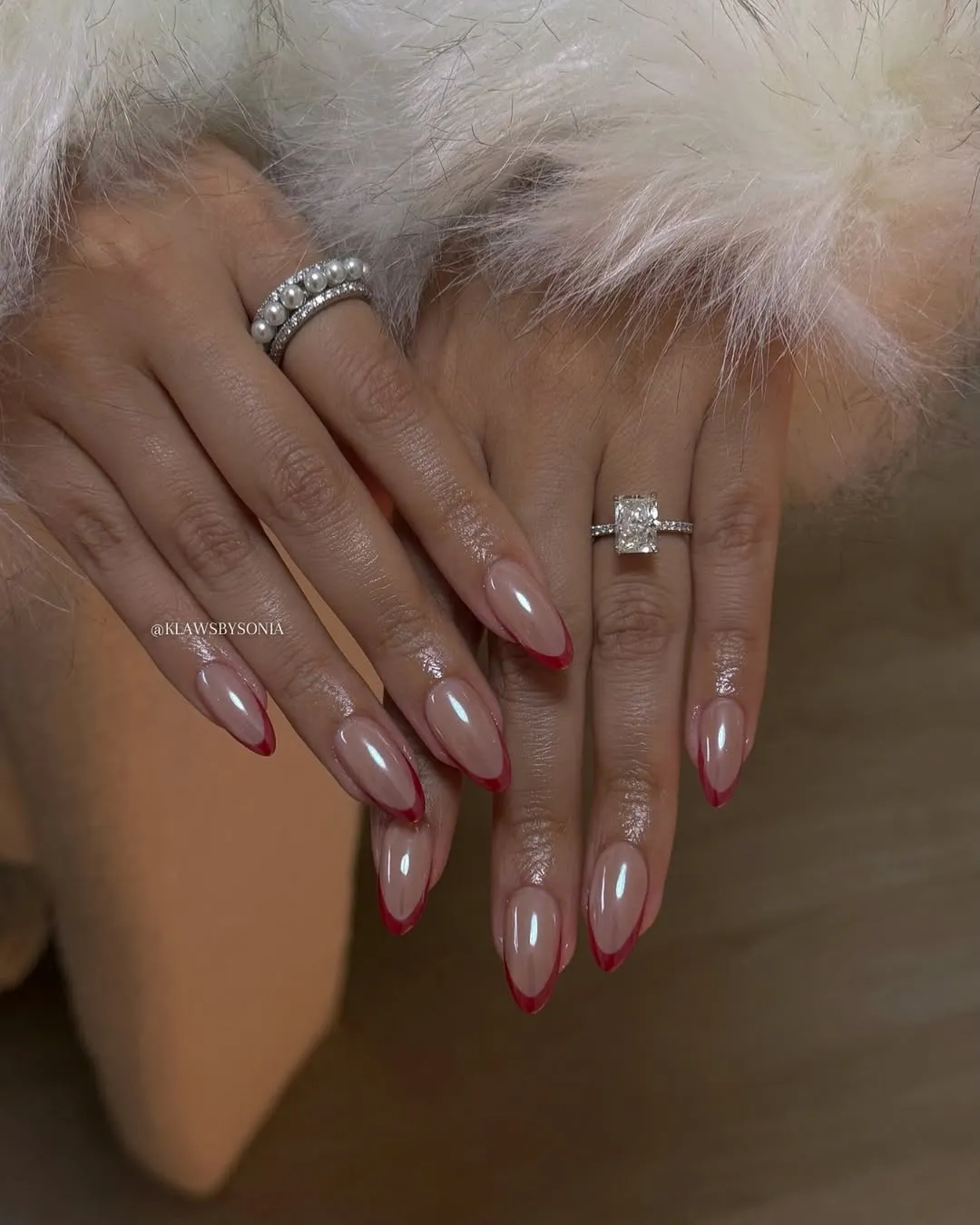 Two hands with elegant manicured nails and rings laid over a fluffy garment