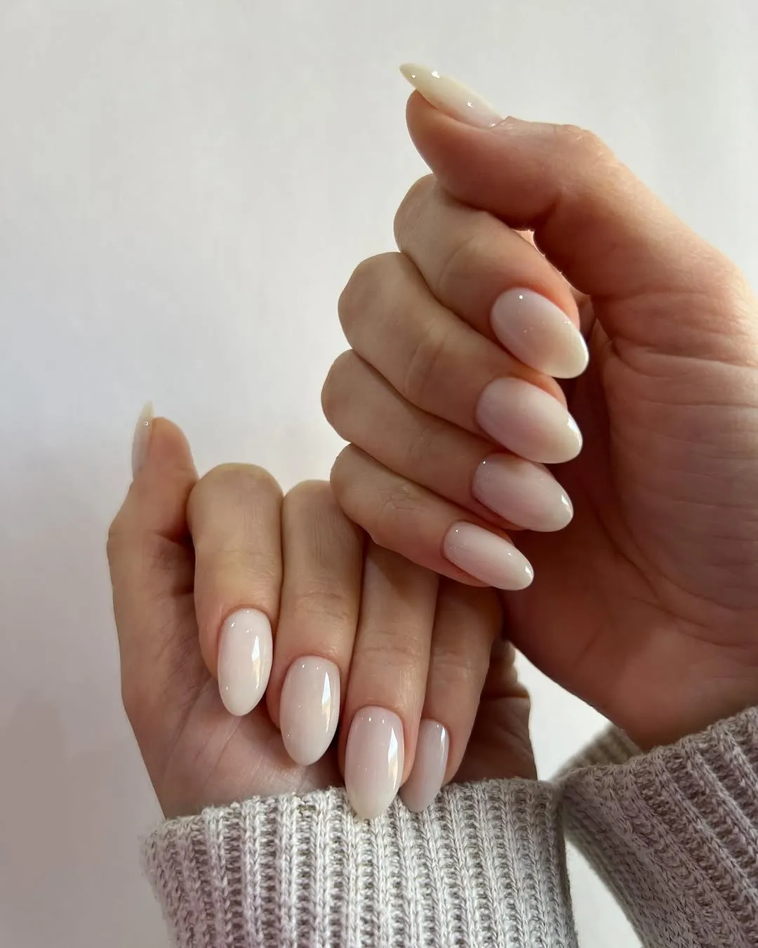 Manicured hands with almondshaped nails in a neutral color sweater sleeves partially visible