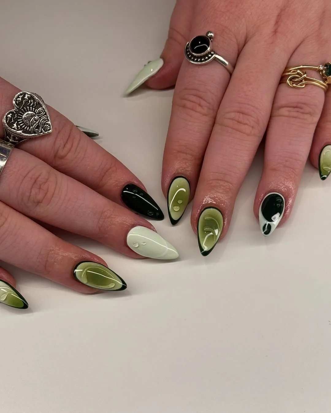 Hands with nail art featuring green patterns and wearing decorative rings