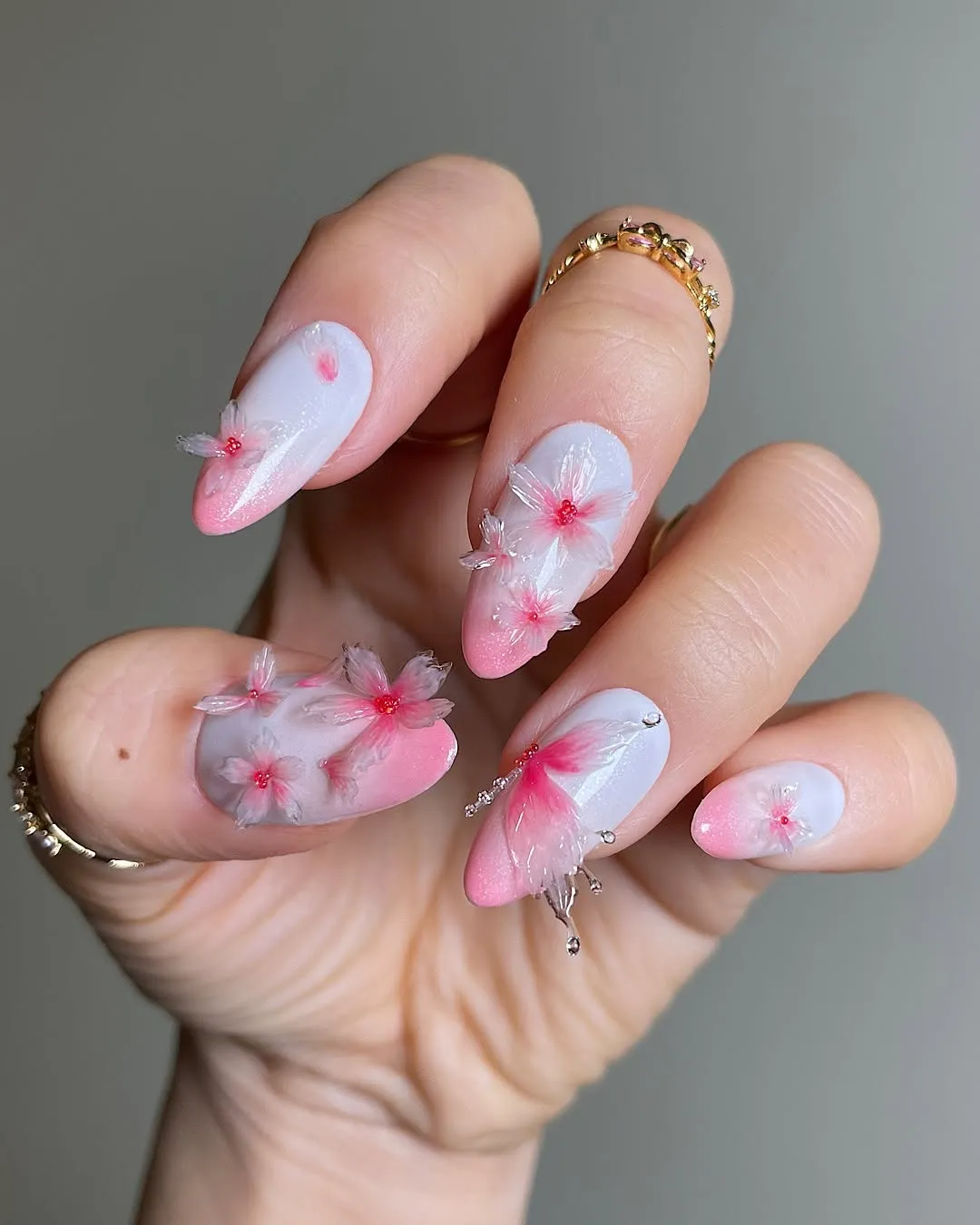 A hand with manicured nails featuring intricate floral designs and embellishments wearing gold rings