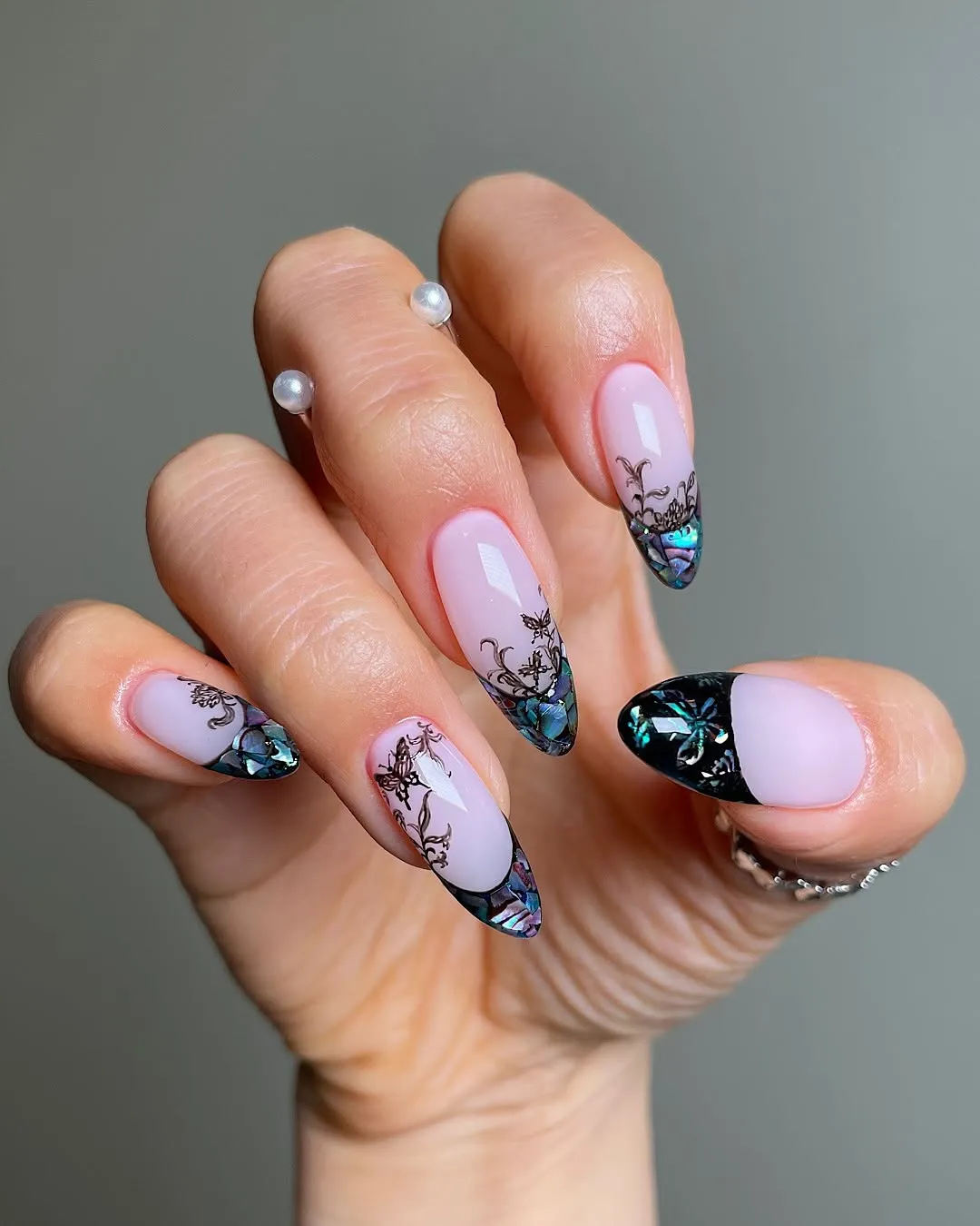 A hand displaying nail art with intricate designs using black and teal embellishments on a light pink base