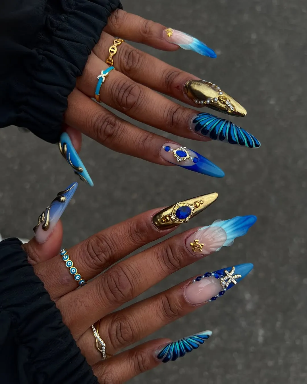 Person with long, stiletto-shaped nails that are blue and gold with a Pisces-inspired vibe