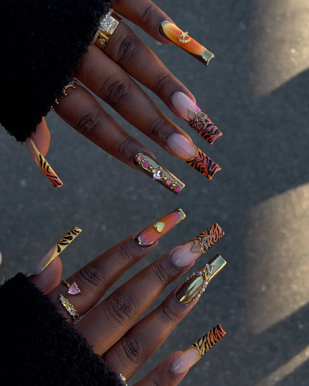 Prson with long, orange, square-shaped nails with tiger stripes and gems