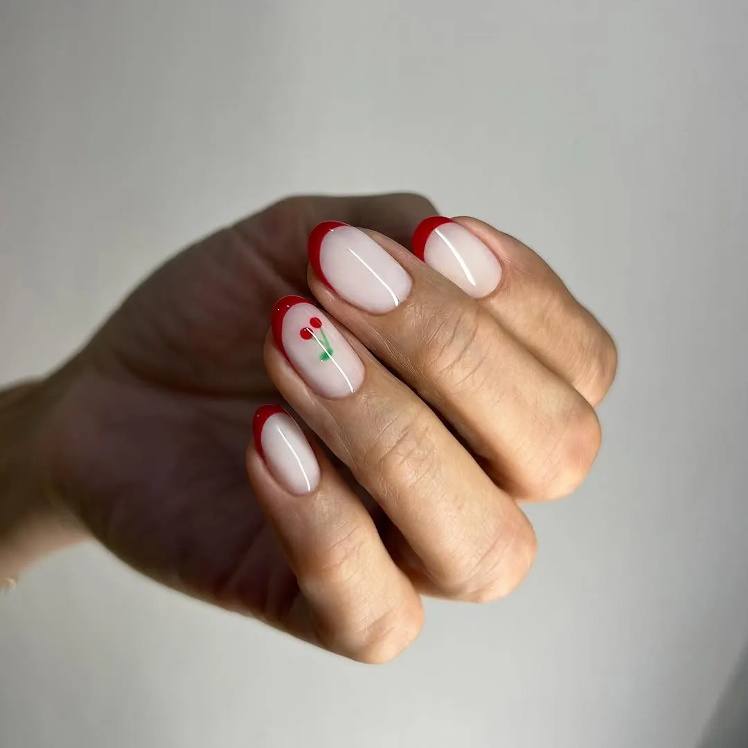 A hand displaying nails with red French tips and a cherry design on one nail