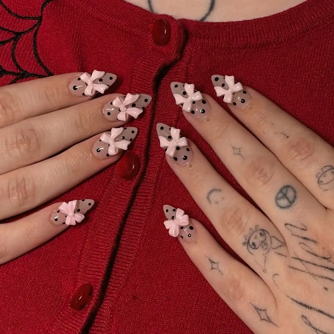 Black and nude polka dot nails with large pink bow charms