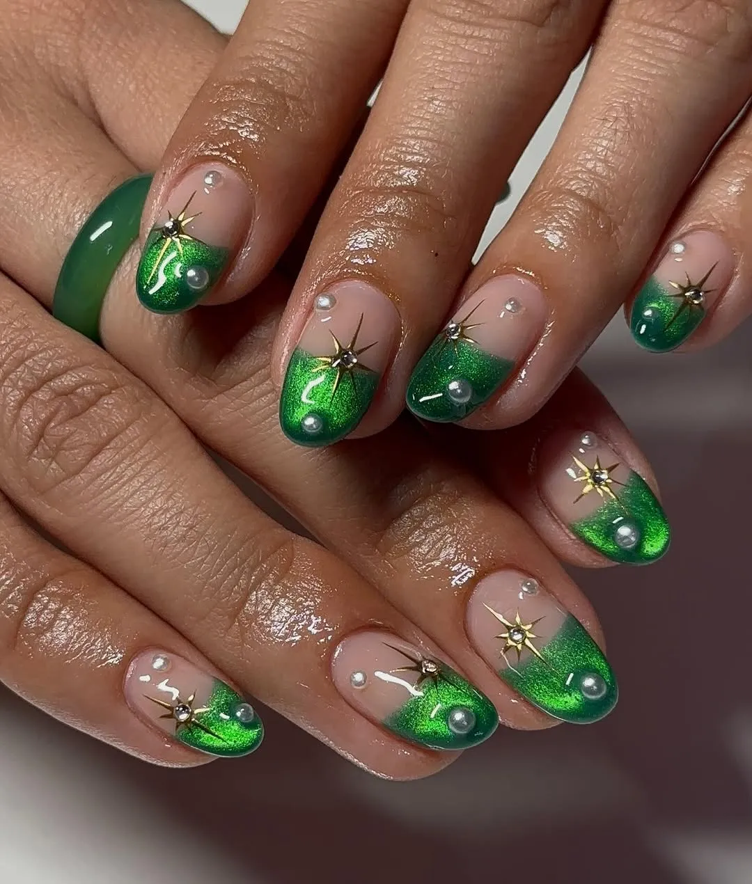 Short nude nails with metallic green French tips and pearl embellishments