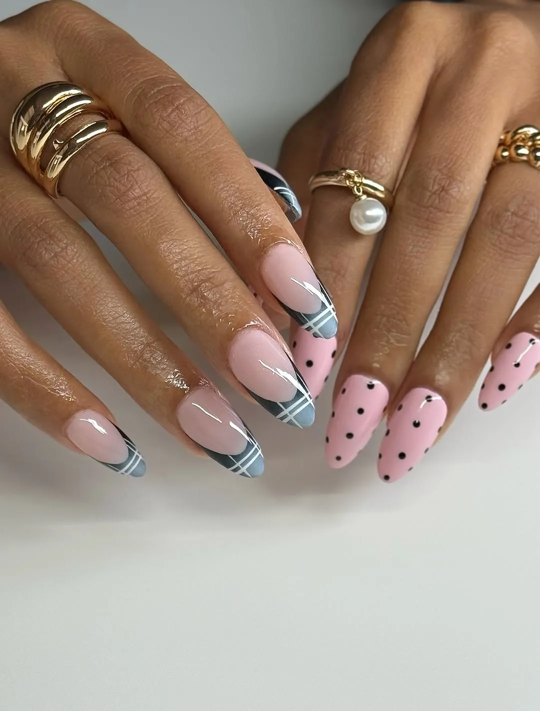 Nails with gray plaid French tips on one hand and pink polka dots on the other
