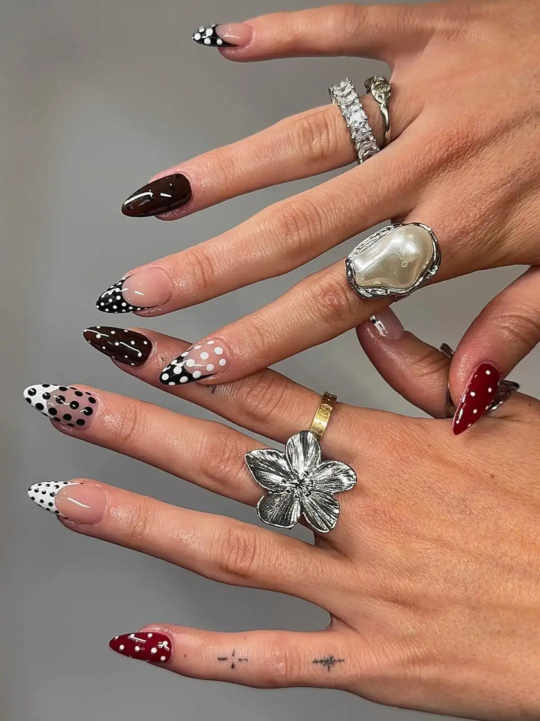 Hands with pointed nails painted in polkadot designs and adorned with rings