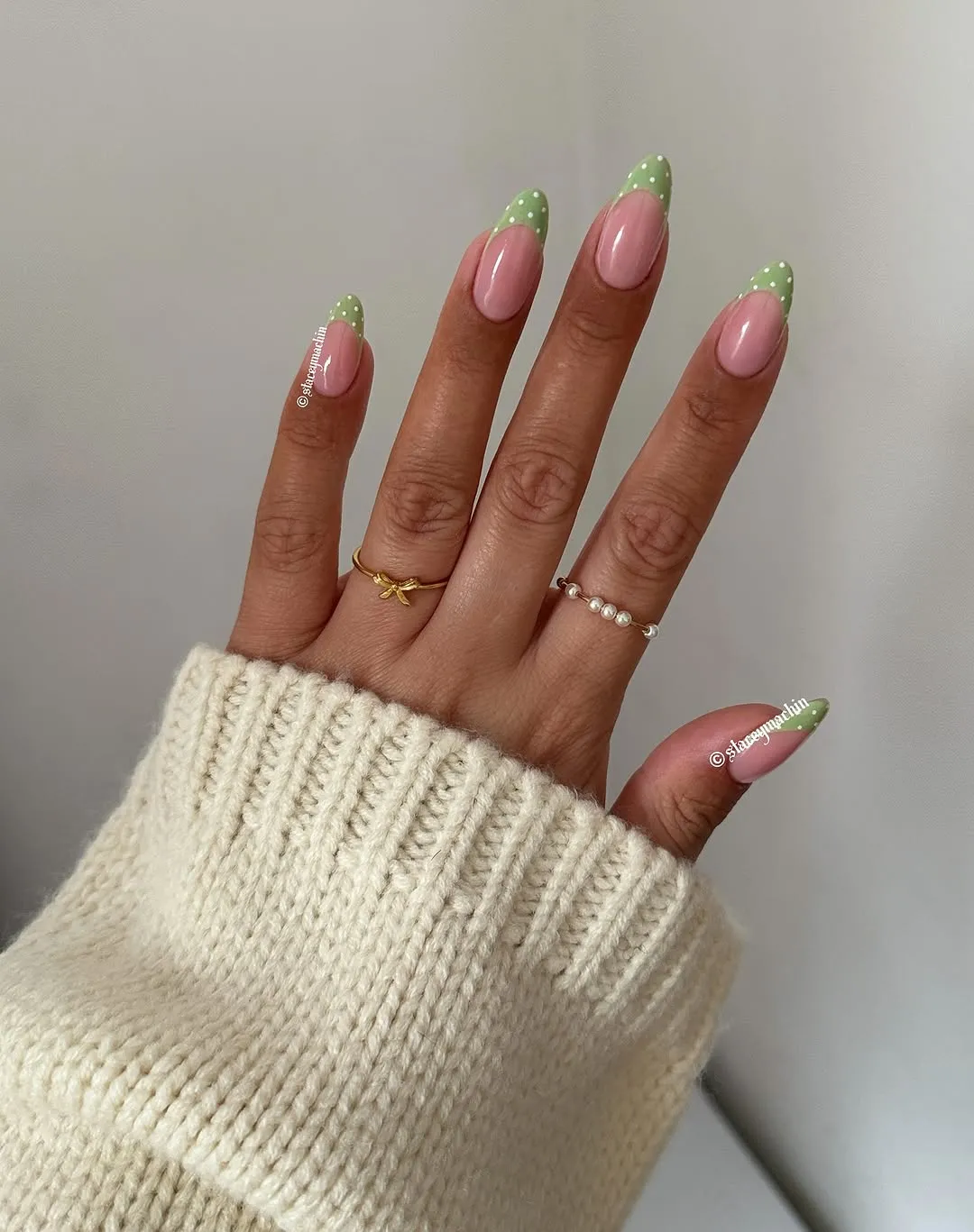A hand wearing rings with manicured nails featuring green and pink designs