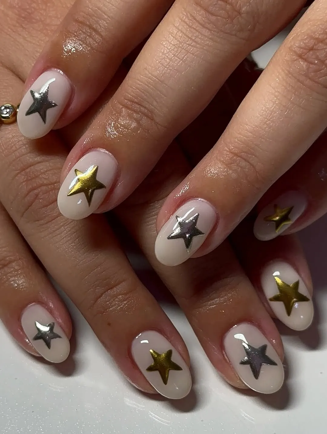 Milky white nails with alternating silver and gold stars on each finger