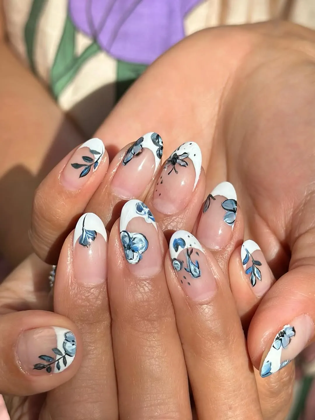 Hands with detailed nail art featuring floral patterns and white and blue designs