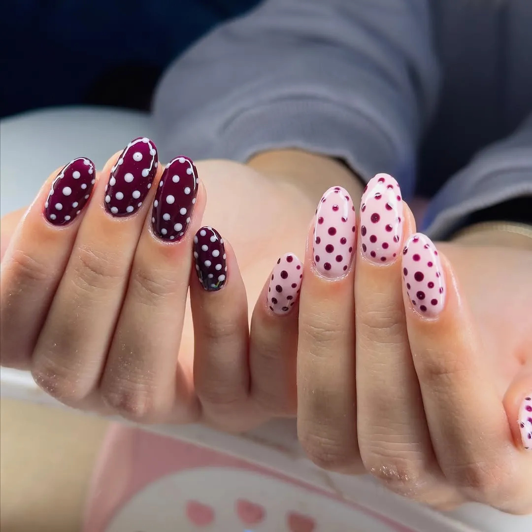 Two hands with polka dot nail designs in contrasting colors (pink and berry)