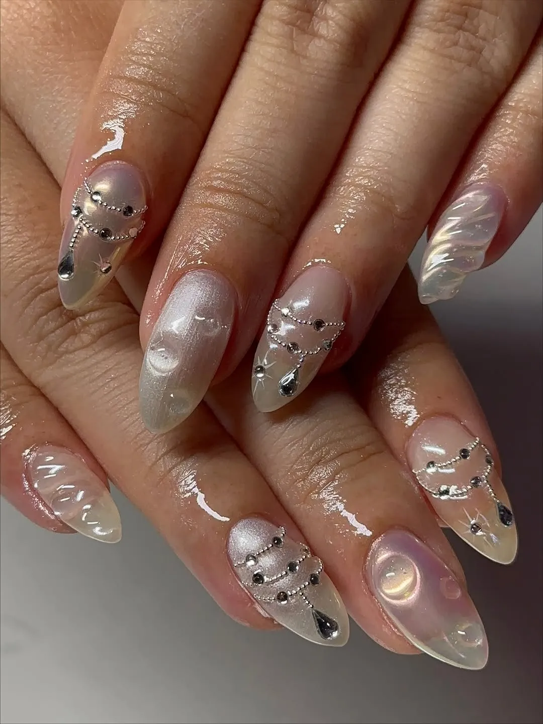 Closeup of manicured hands with decorative nail art featuring shiny accents and intricate patterns on almond-shaped nails
