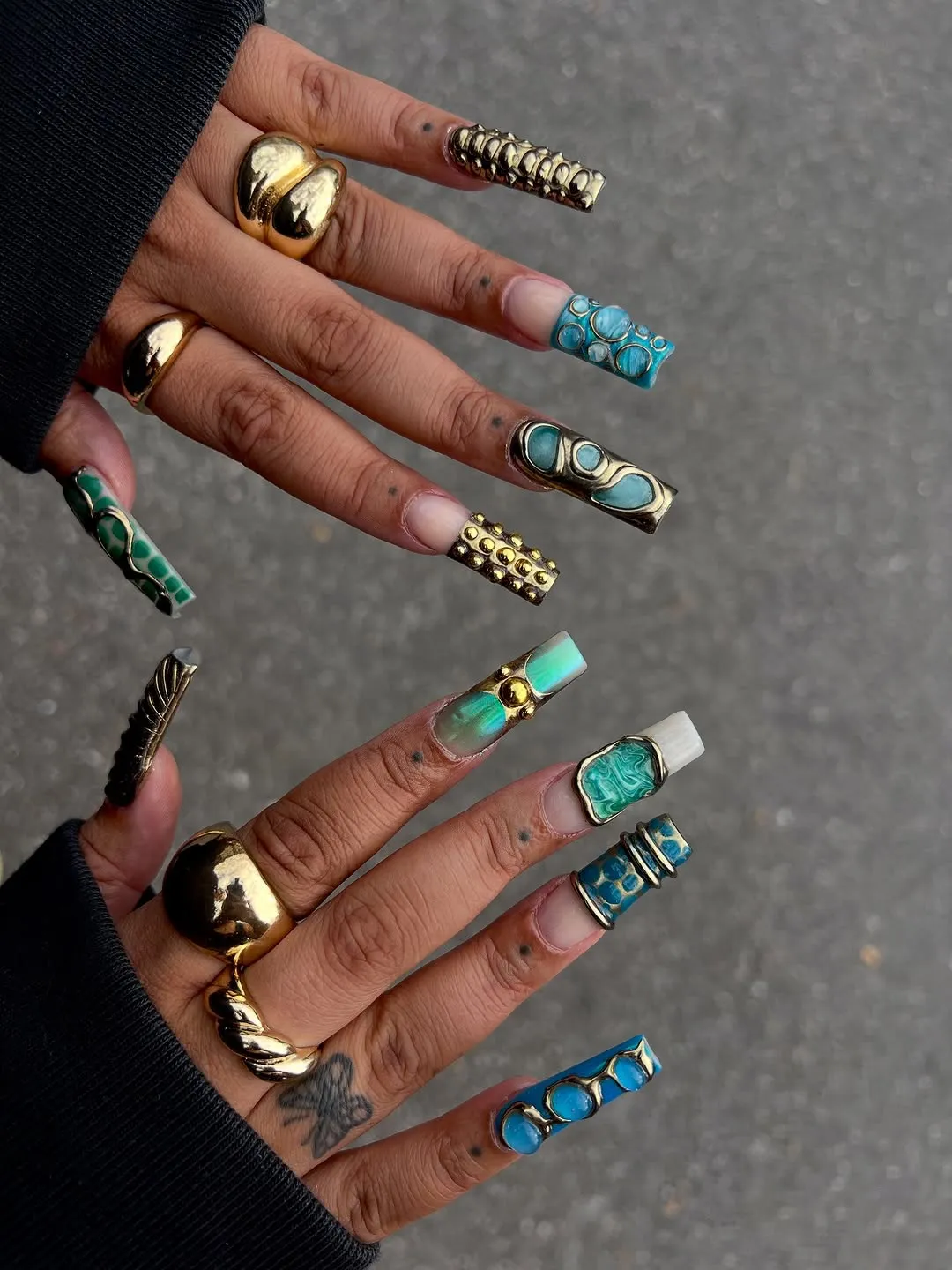Person with long, square-shaped nails in blue and green tones with gold metallic nails