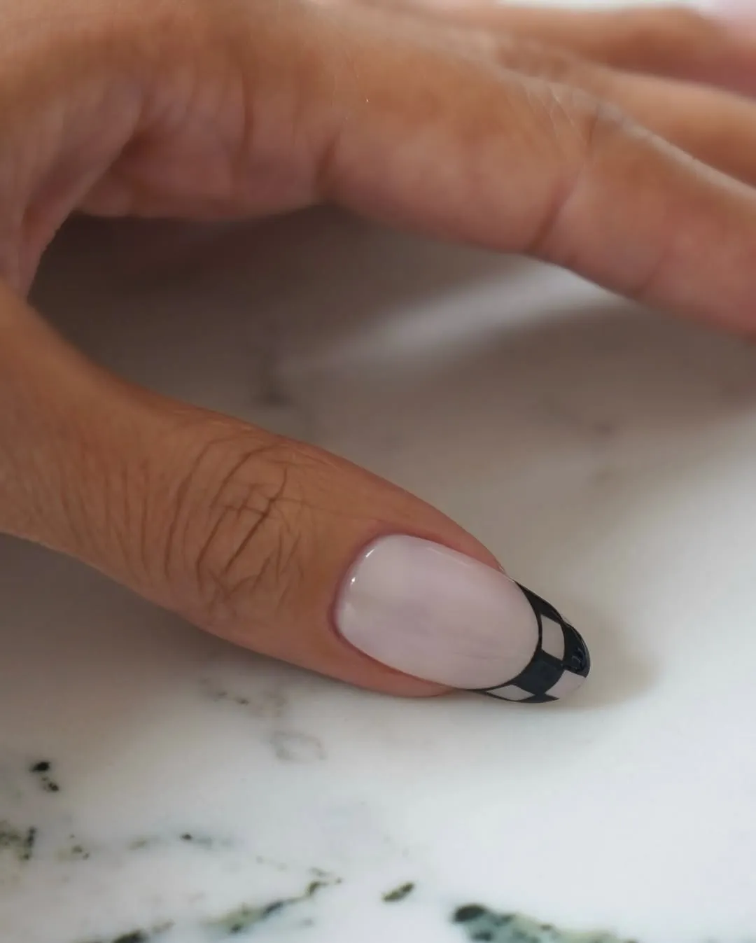 A closeup of a hand resting on a surface showing detailed nail art with a patterned design on one fingernail