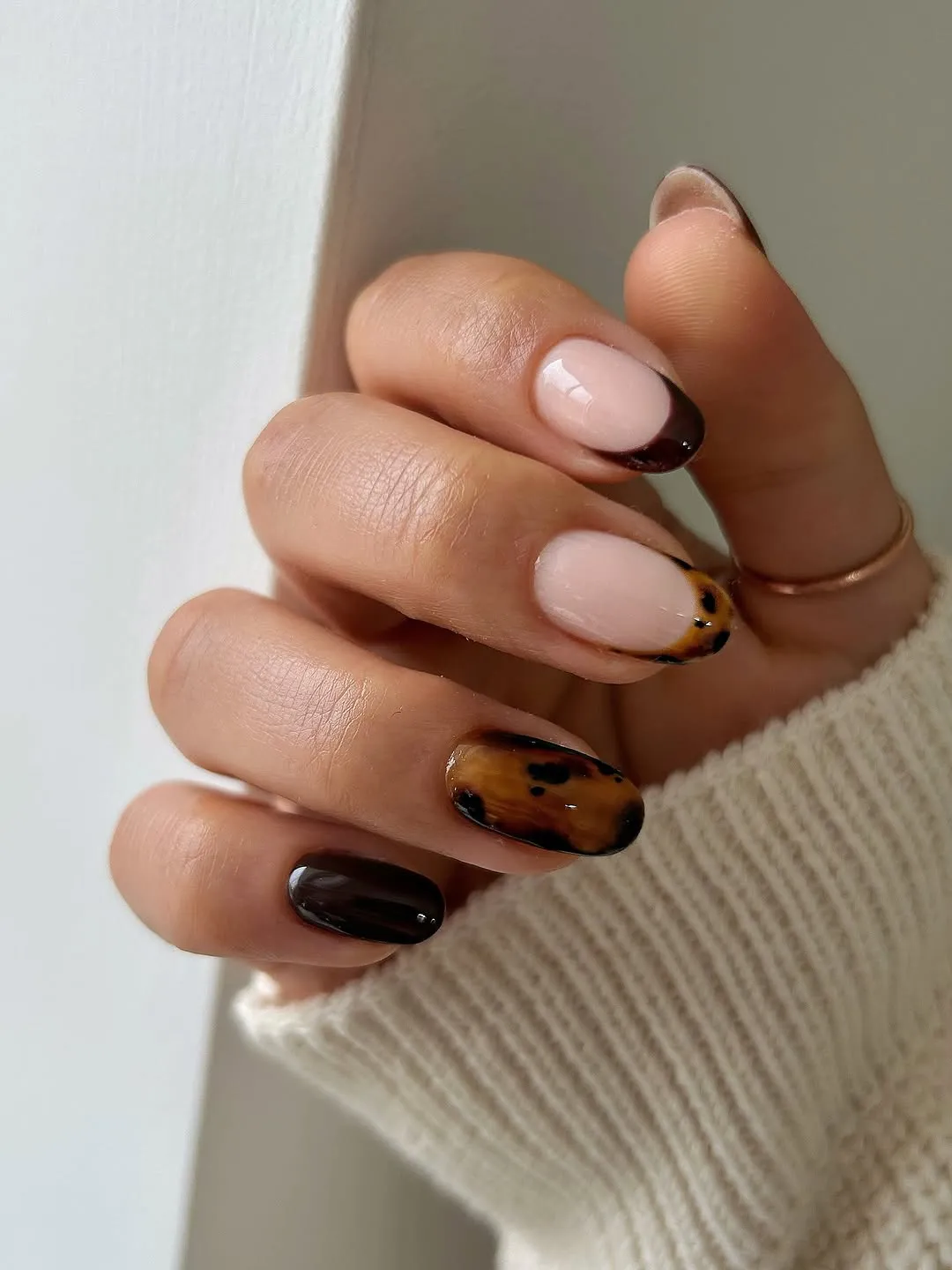 A hand with decorated fingernails in a variety of styles including solid and tortoiseshell patterns