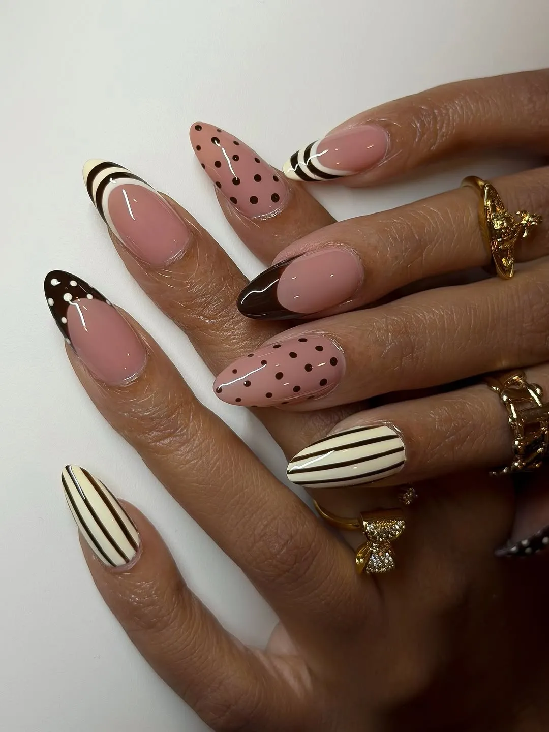 Closeup of hands with decorated nails featuring polka dots stripes and solid designs also wearing several rings
