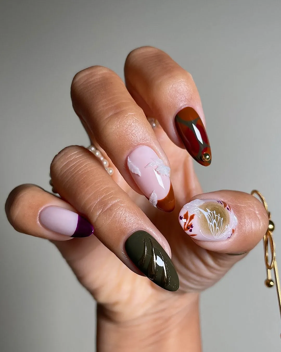 A hand with various artistic nail designs and a bracelet