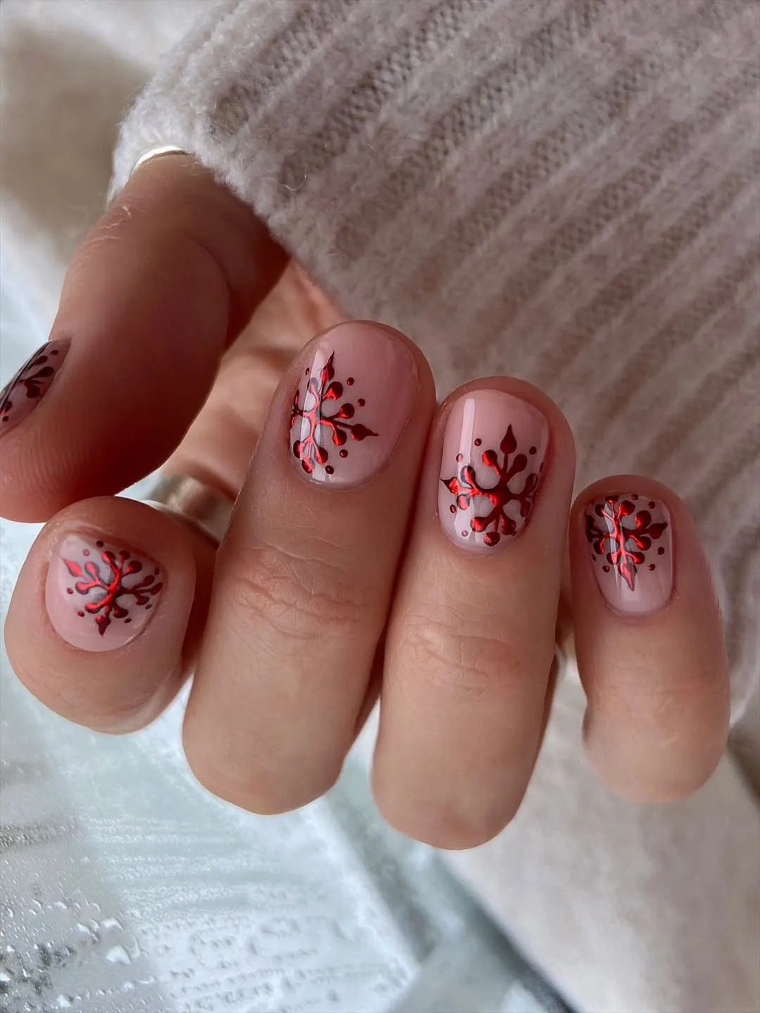 Hand with painted nail art featuring branches and small red dots