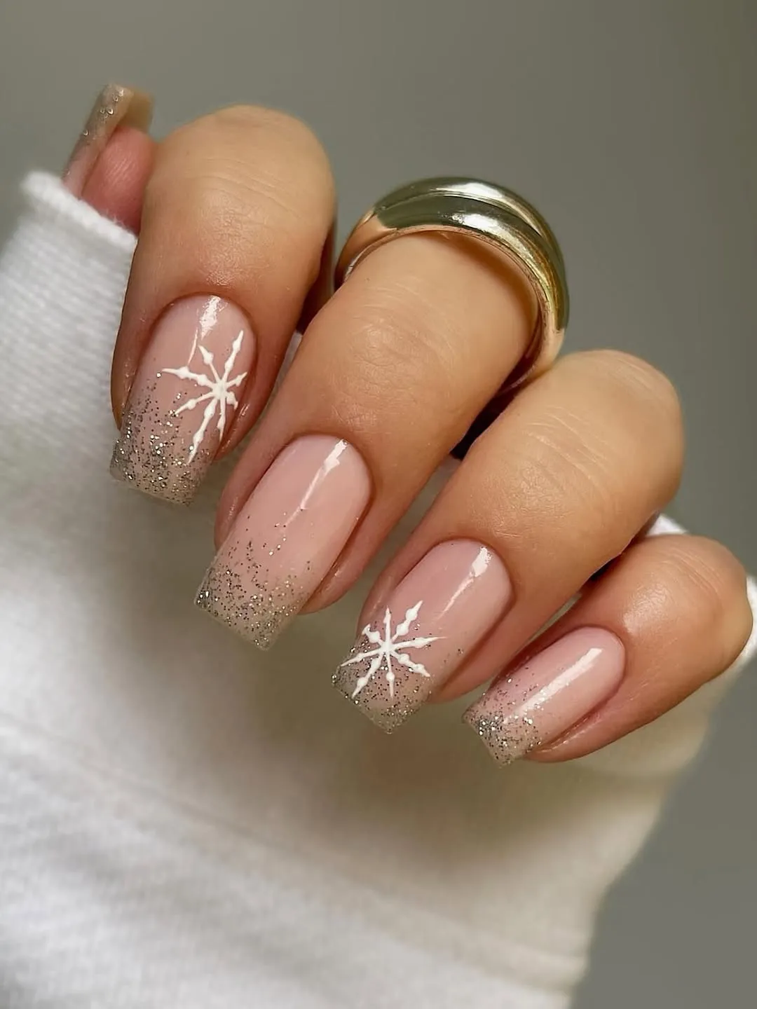 Nude nails with gold glitter ombre and white snowflake accents