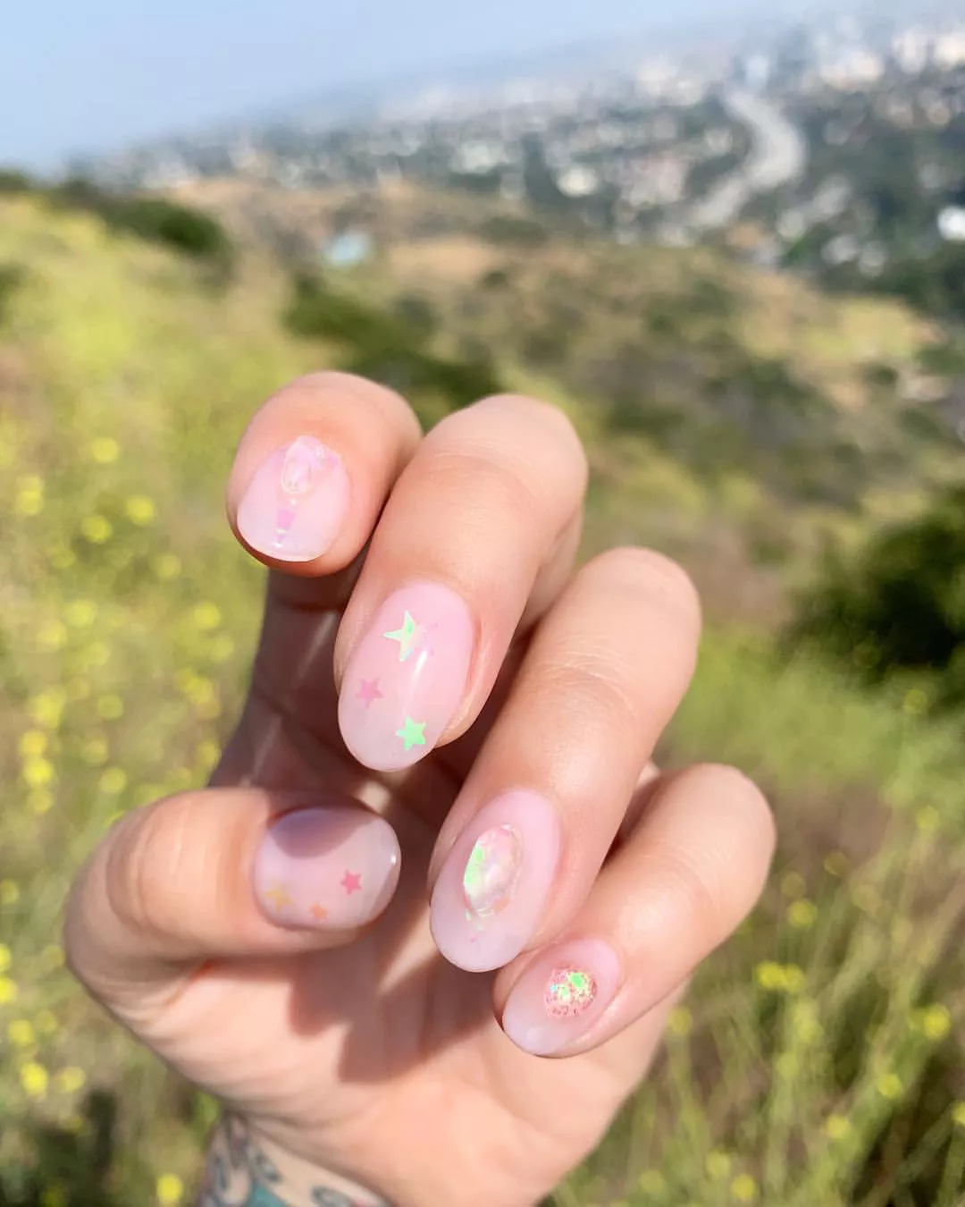 Person with short, pink, round nails that have star decals and iridescent gems