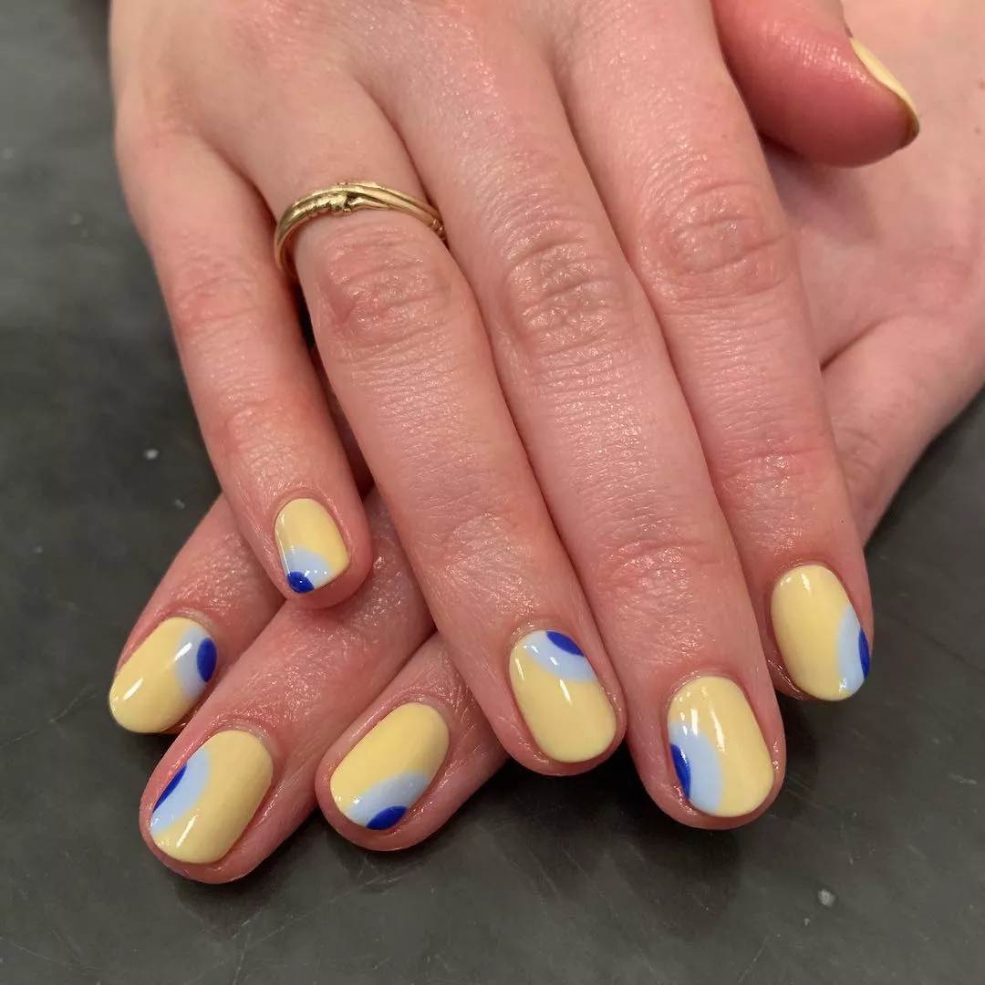 Person with short, oval-shaped nails painted in butter yellow, light blue, and royal blue