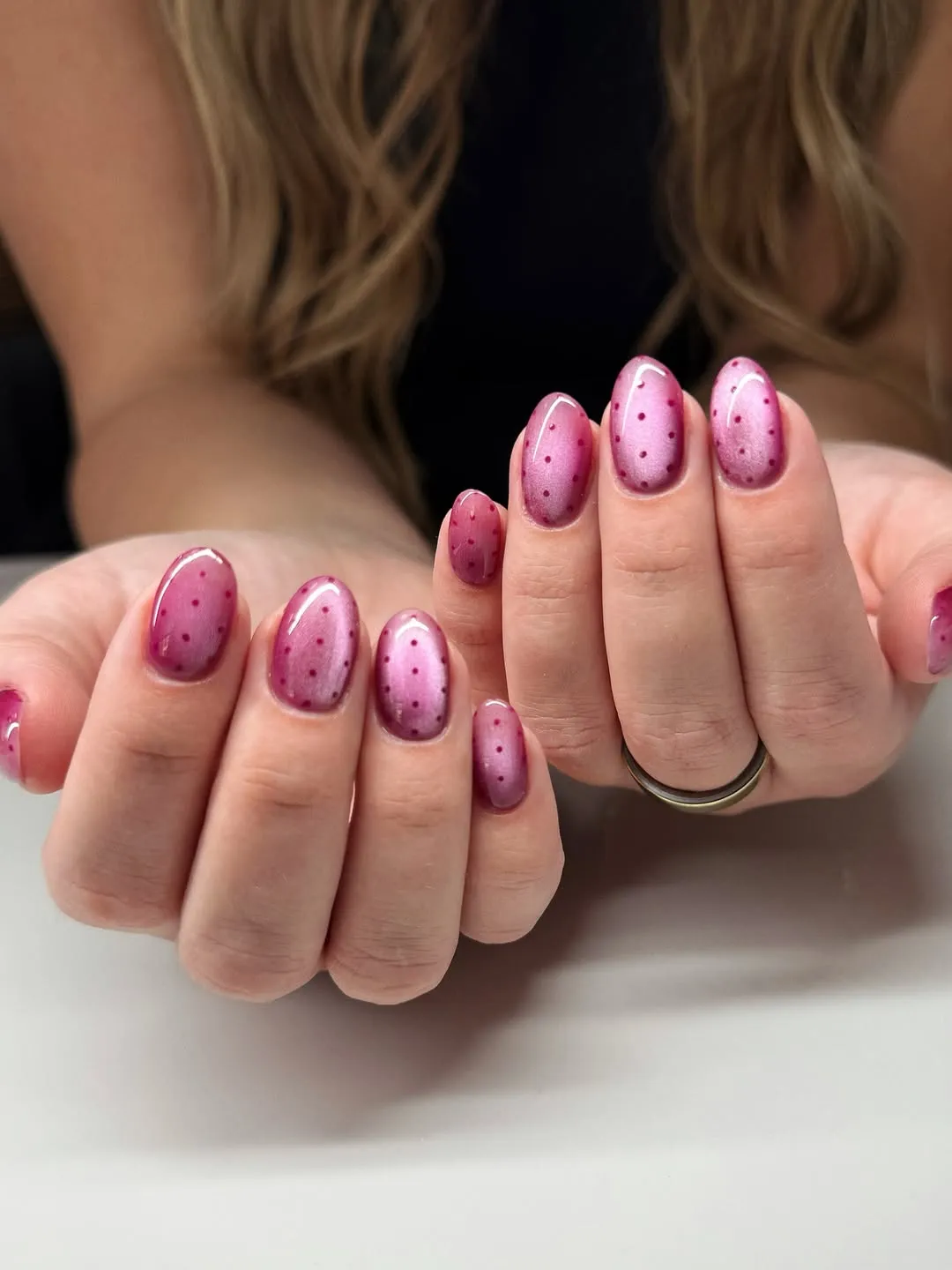 Hands showing nails with a polished design featuring pink tones and dots person has long flowing hair in the background