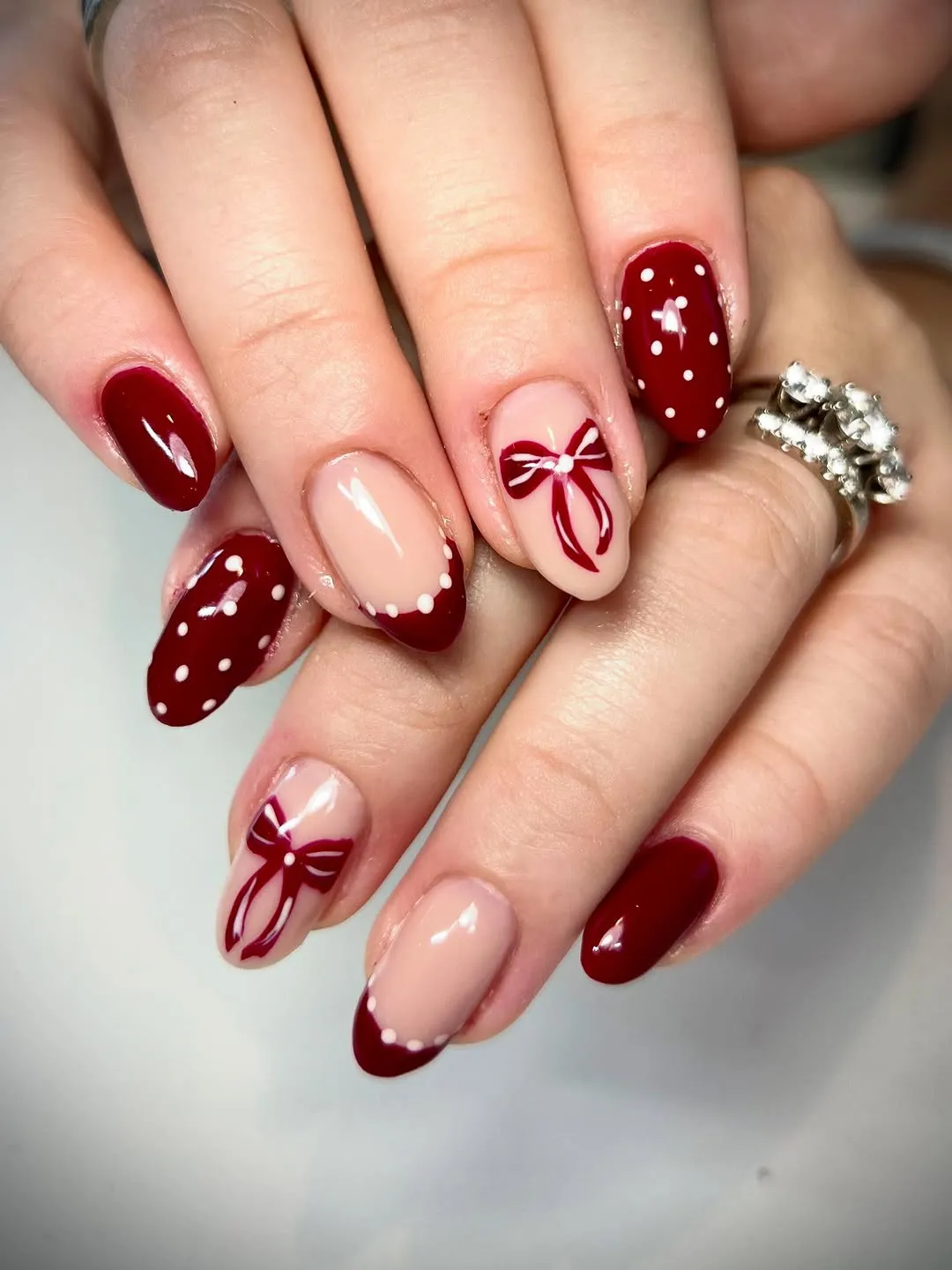 Hands with red and beige nail art decorated with bows and dots