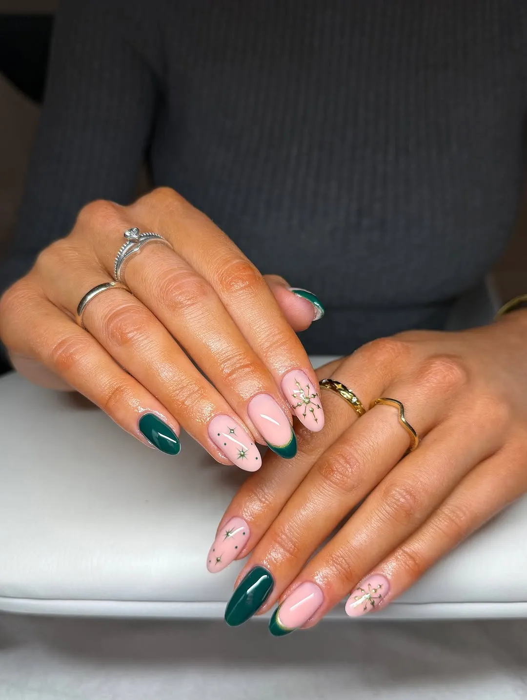 Closeup of hands with manicured nails featuring green and pink designs adorned with rings