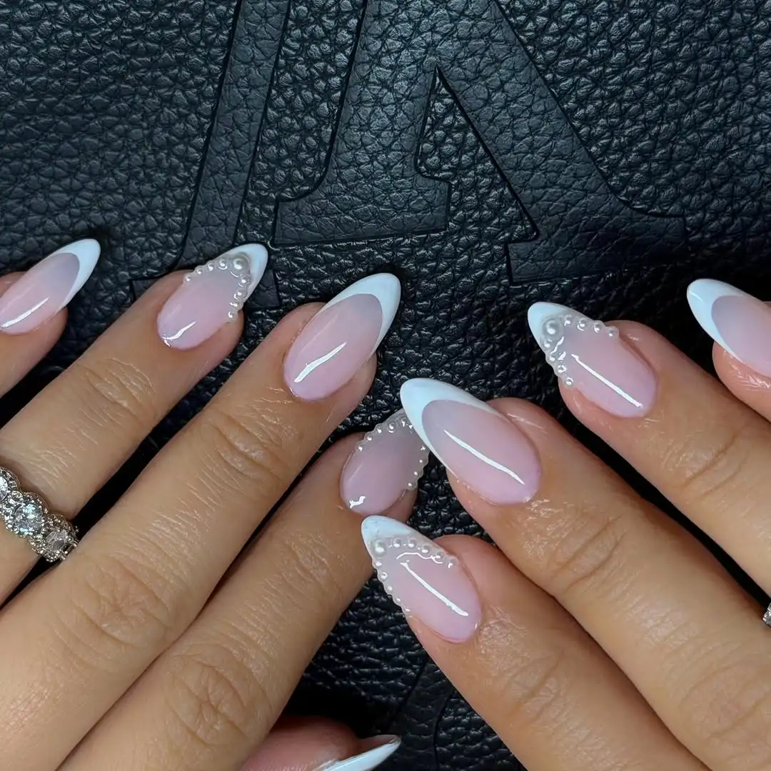 Hands with manicured nails featuring white french tips and gemstone accents resting on a textured surface