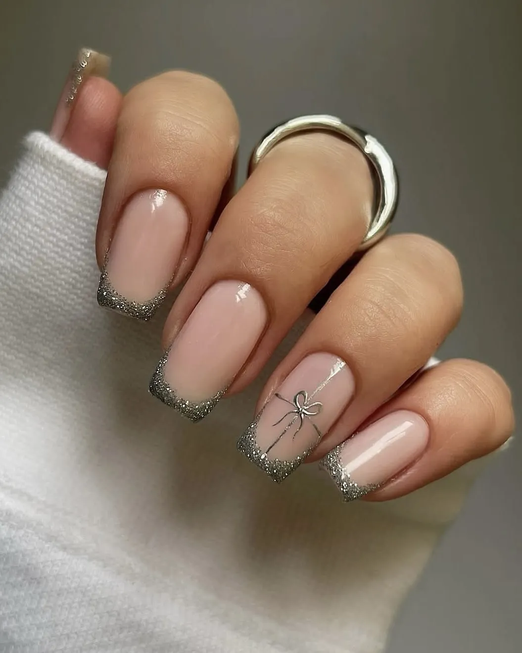Silver French tips and a bow on a glossy neutral manicure.