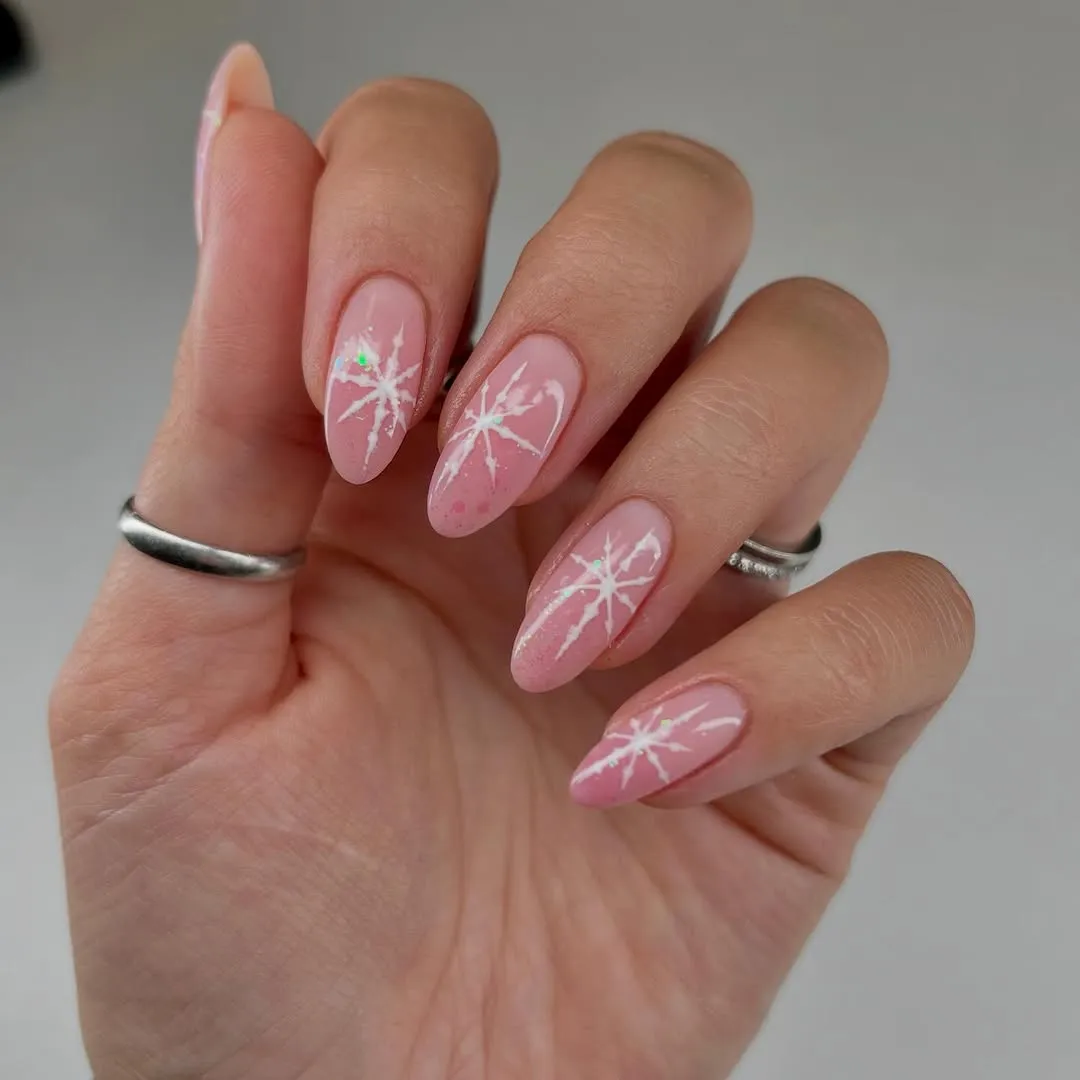 Sheer pink glittery nails with white snowflake accents