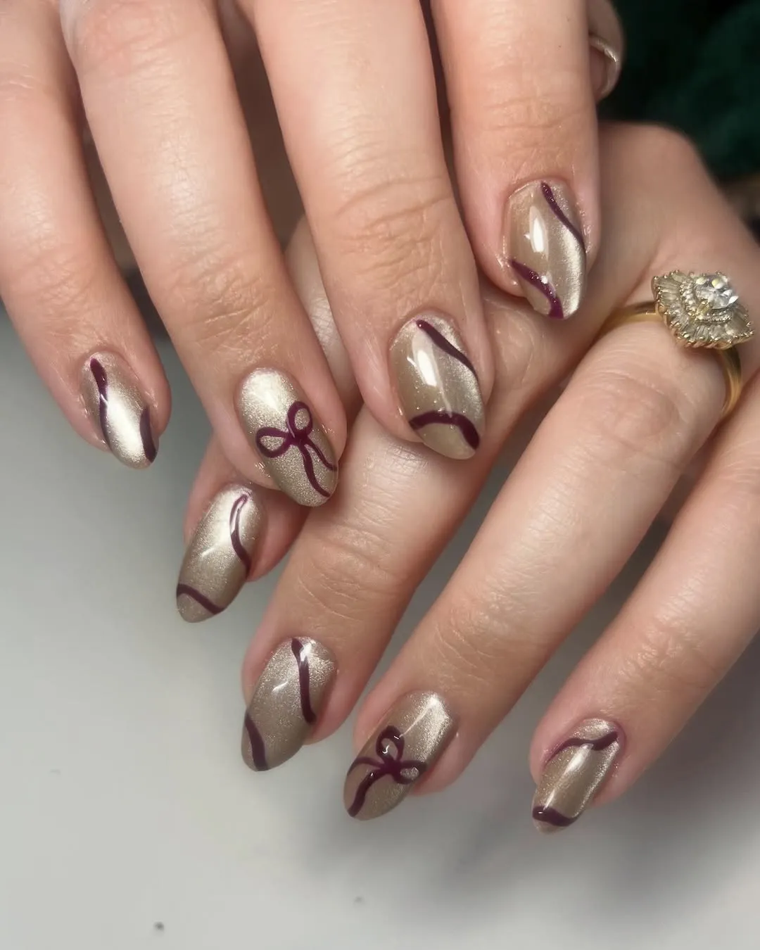 Champagne-colored manicure with burgundy bow and ribbon art.