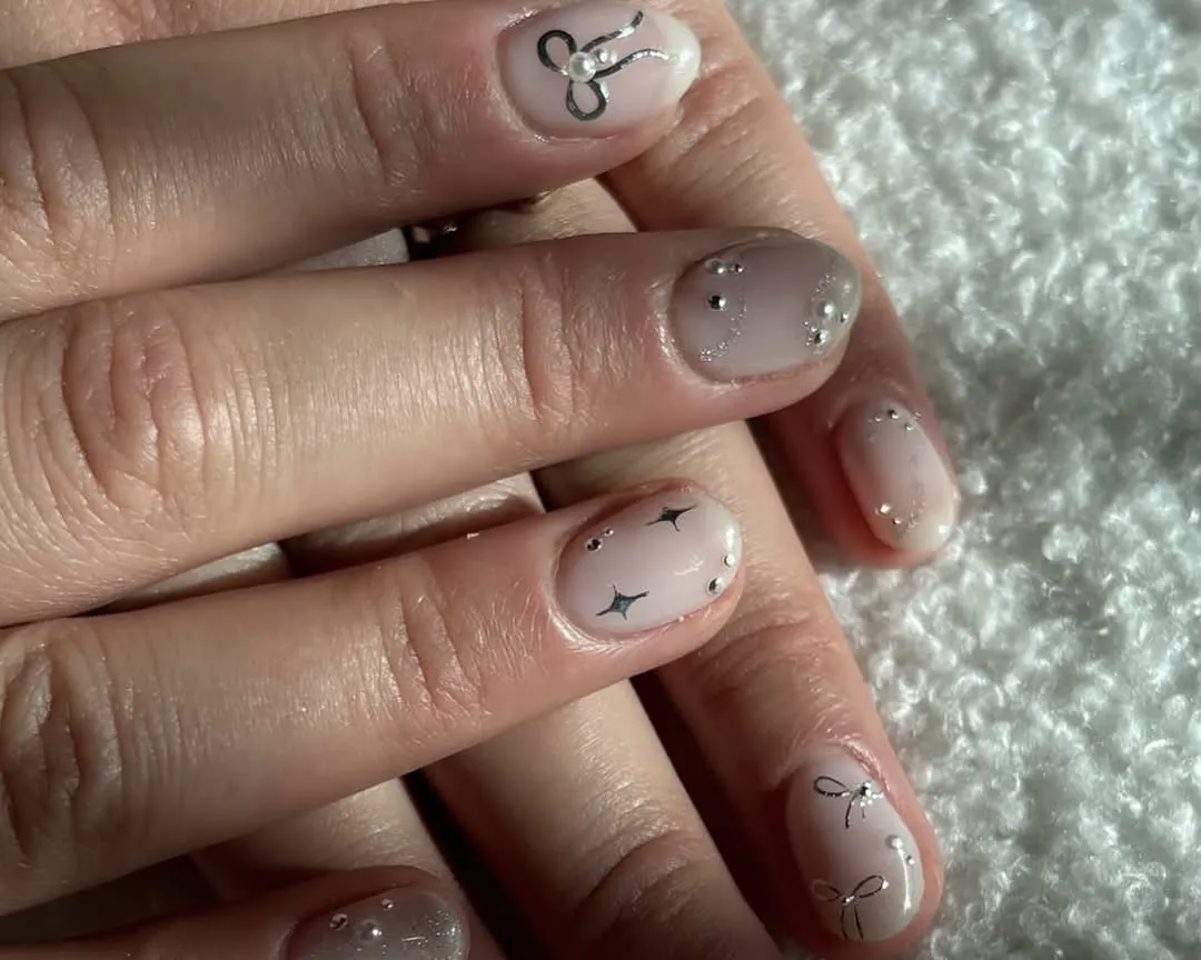 Sheer beige nails with silver chrome accents like bows and twinkles.