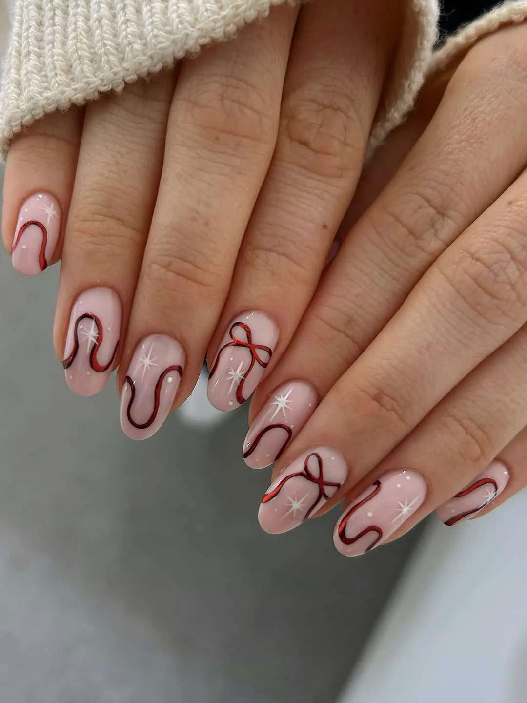 Hands with manicure featuring nail art with curved lines and ribbon designs