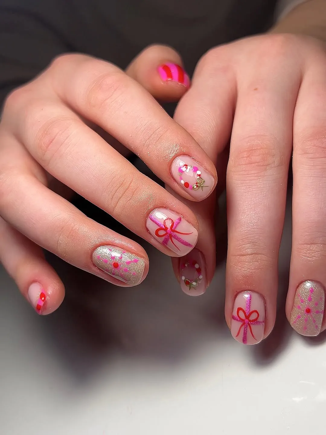 A persons hands showing nail art featuring pink bows and floral designs on a white background