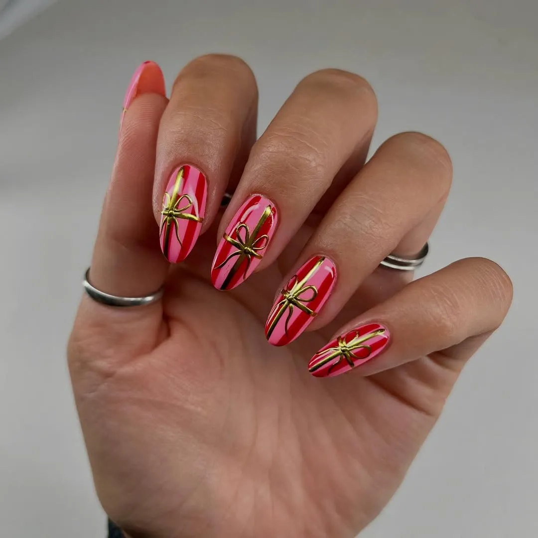 Pink and red striped nails with gold chrome bow accents
