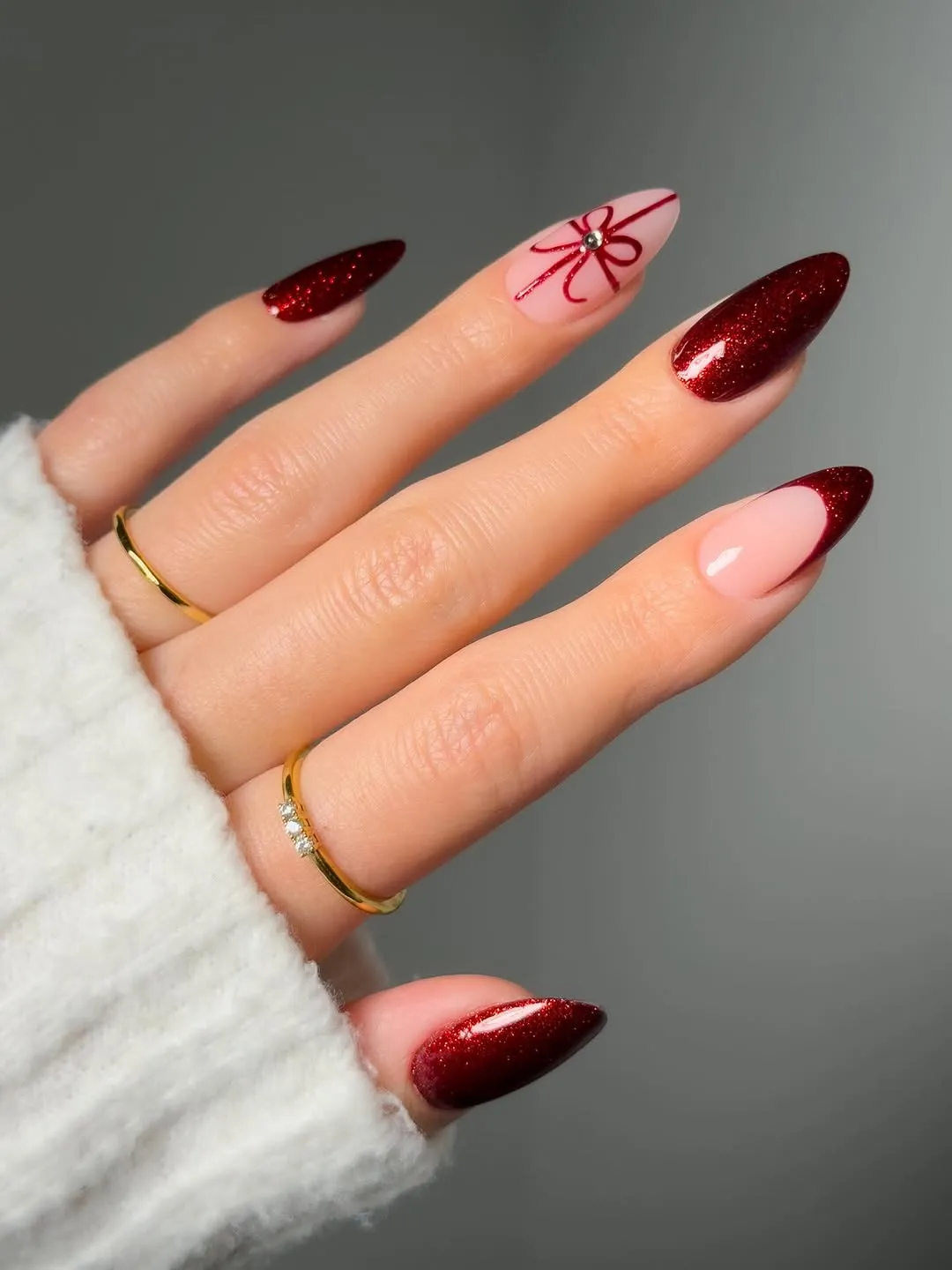 Hand with glittery red nails and a holiday-themed design on one nail