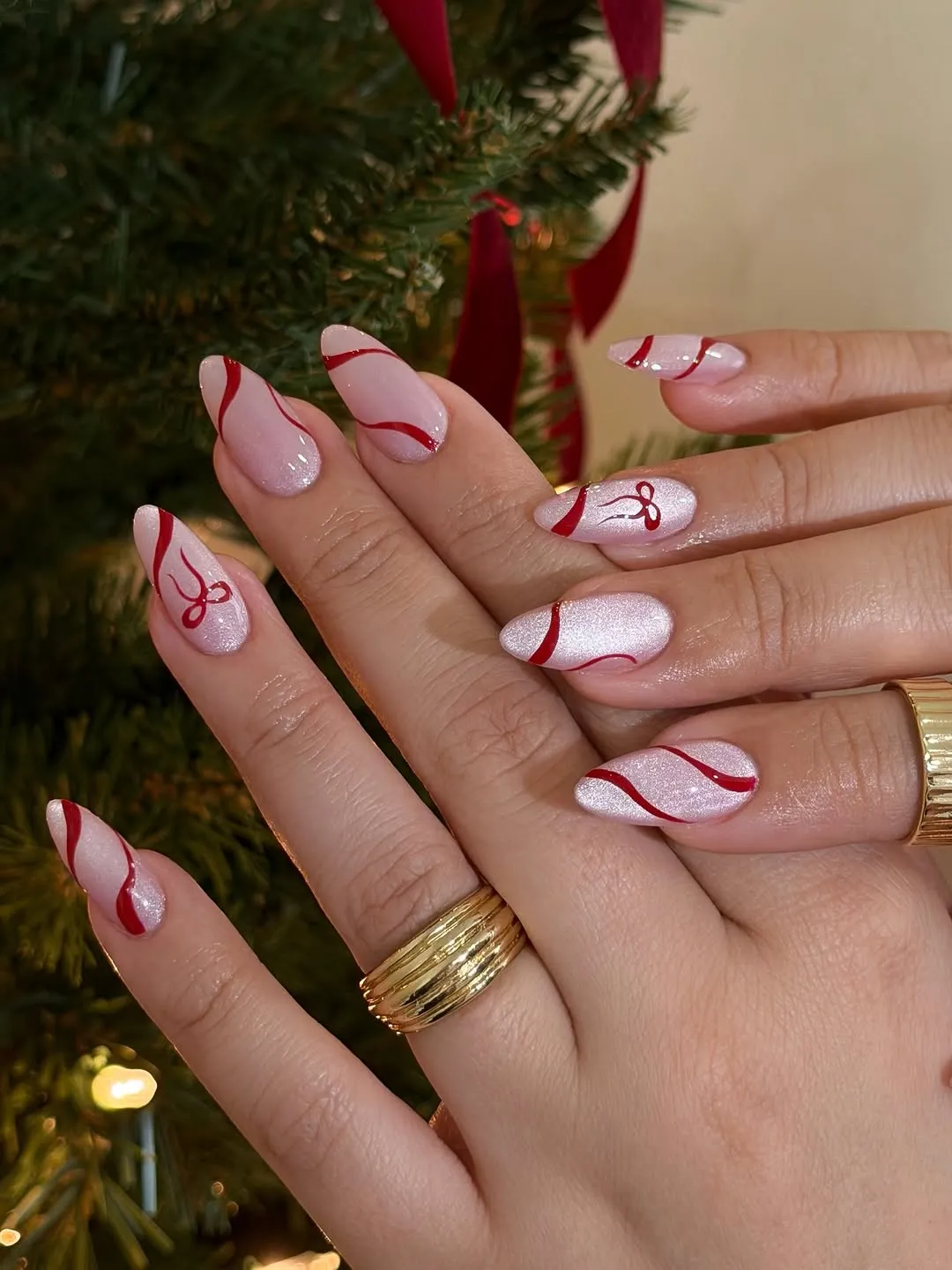 Hands with festive nail art featuring candycane stripes near a Christmas tree