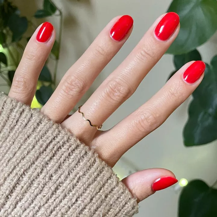 Person with short, round nails painted in a sheer bright red nail polish