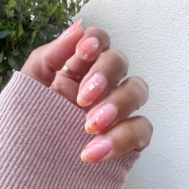 Person shows off their short, oval-shaped nails that are sheer with gold flakes