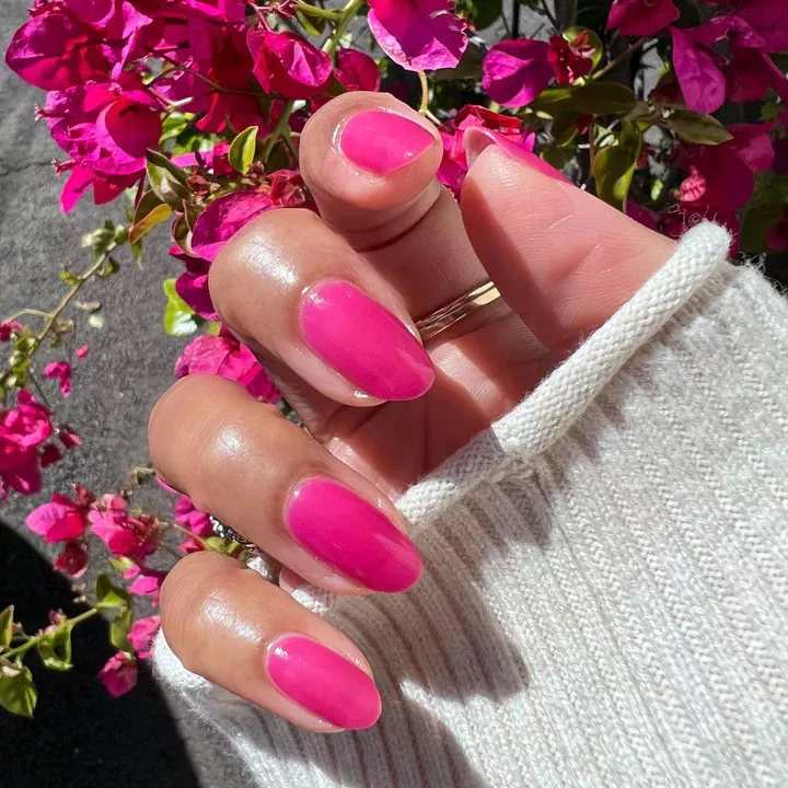 A person showing off their manicure in a translucent hot pink shade and almond shape