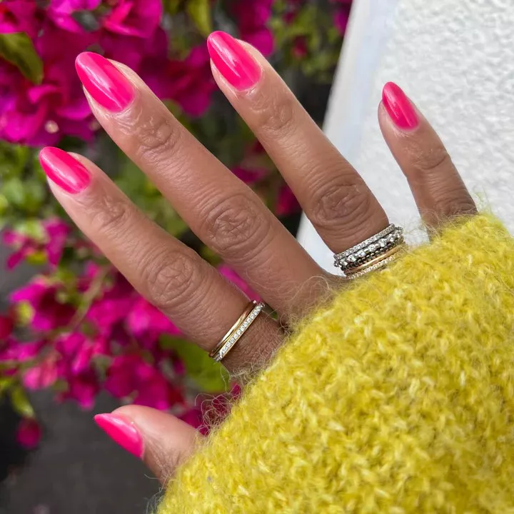 Person wearing a glossy hot pink polish on their short, oval-shaped nails