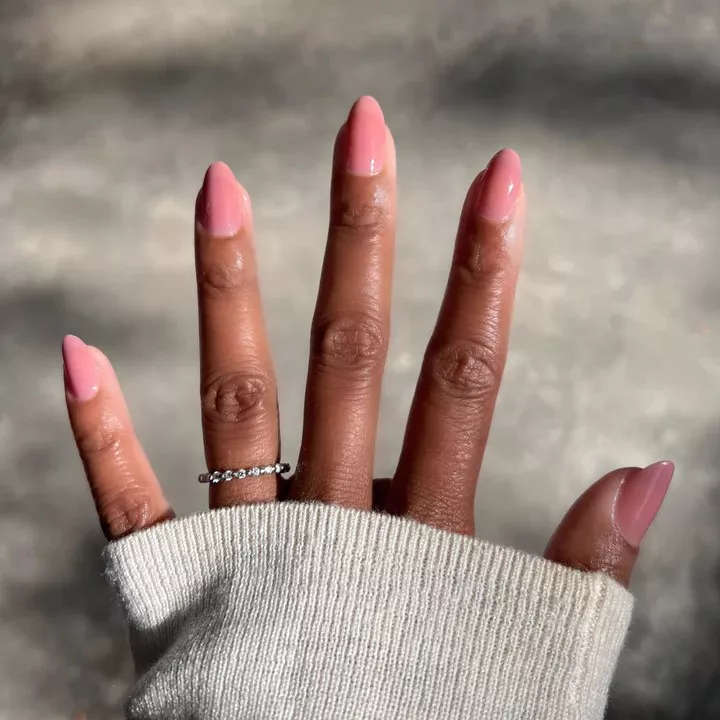 Person with oval-shaped nails painted in a sheer medium-dark pink