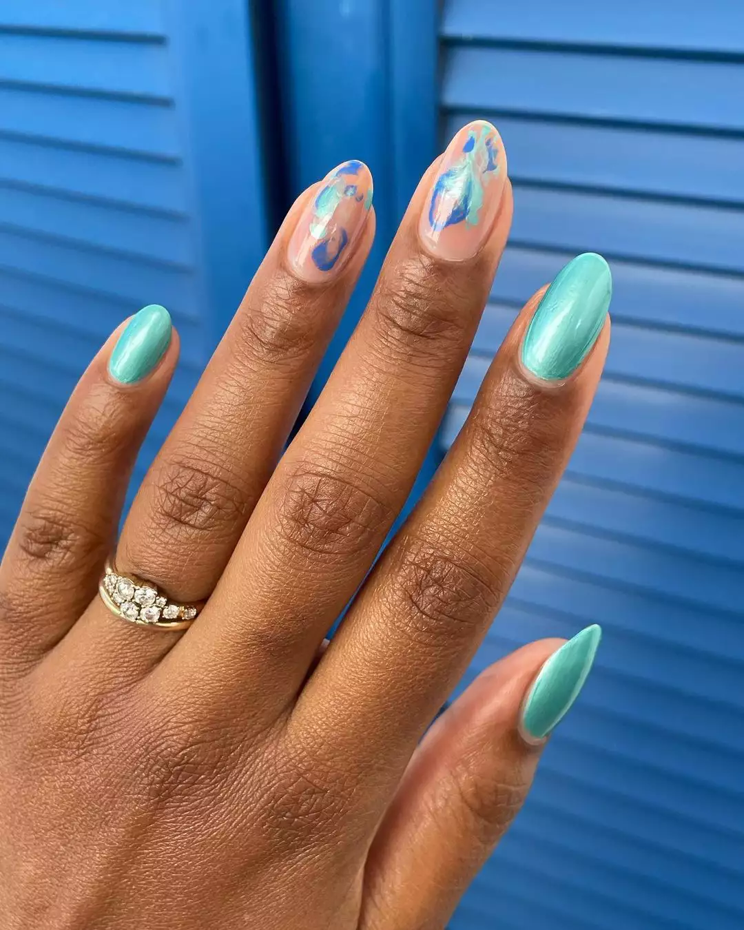 Person showing off their round nails that are painted in blue chrome polish with marbled accents